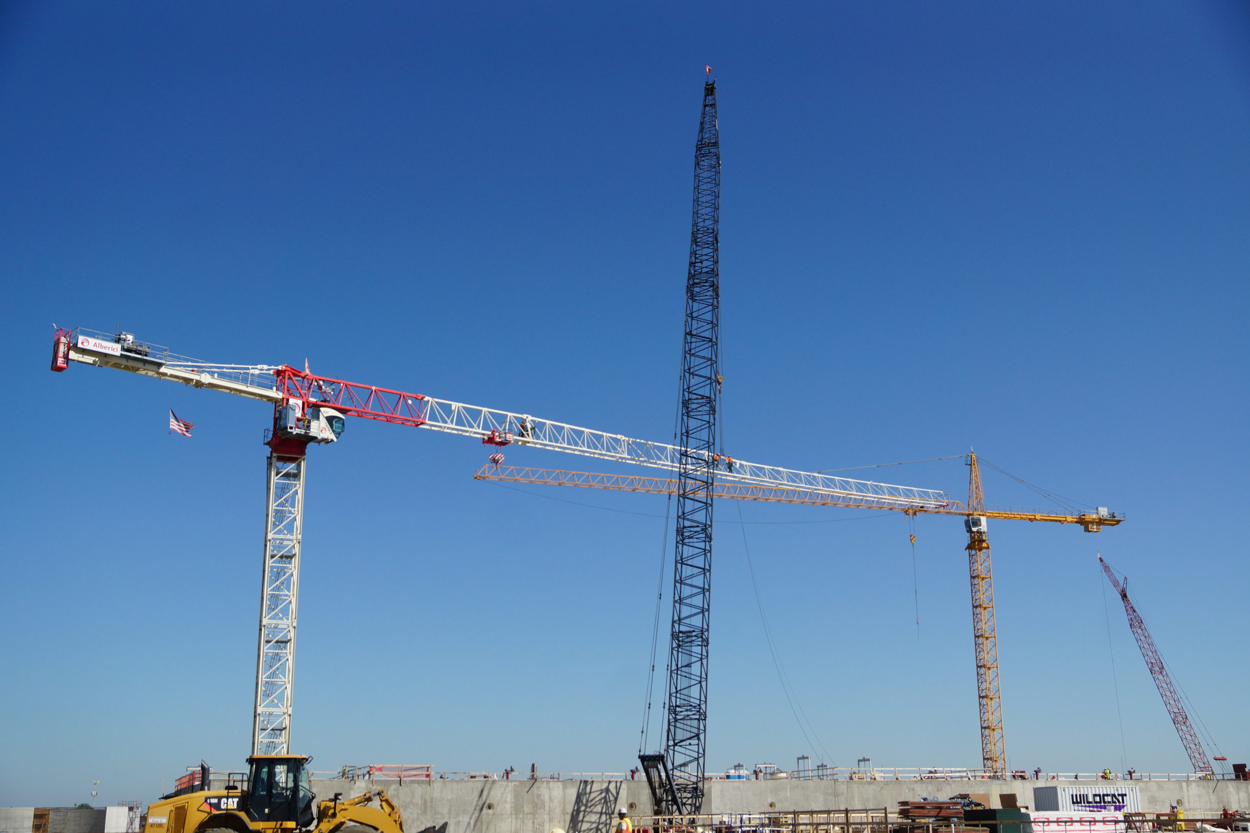 Image of tower crane flanked by another crane that will aid in dismantling it.