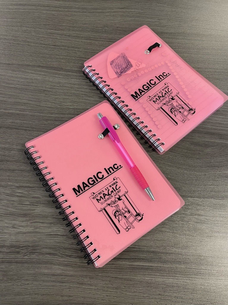 Photo shows two, small pink notebooks with the MAGIC Camp logo 